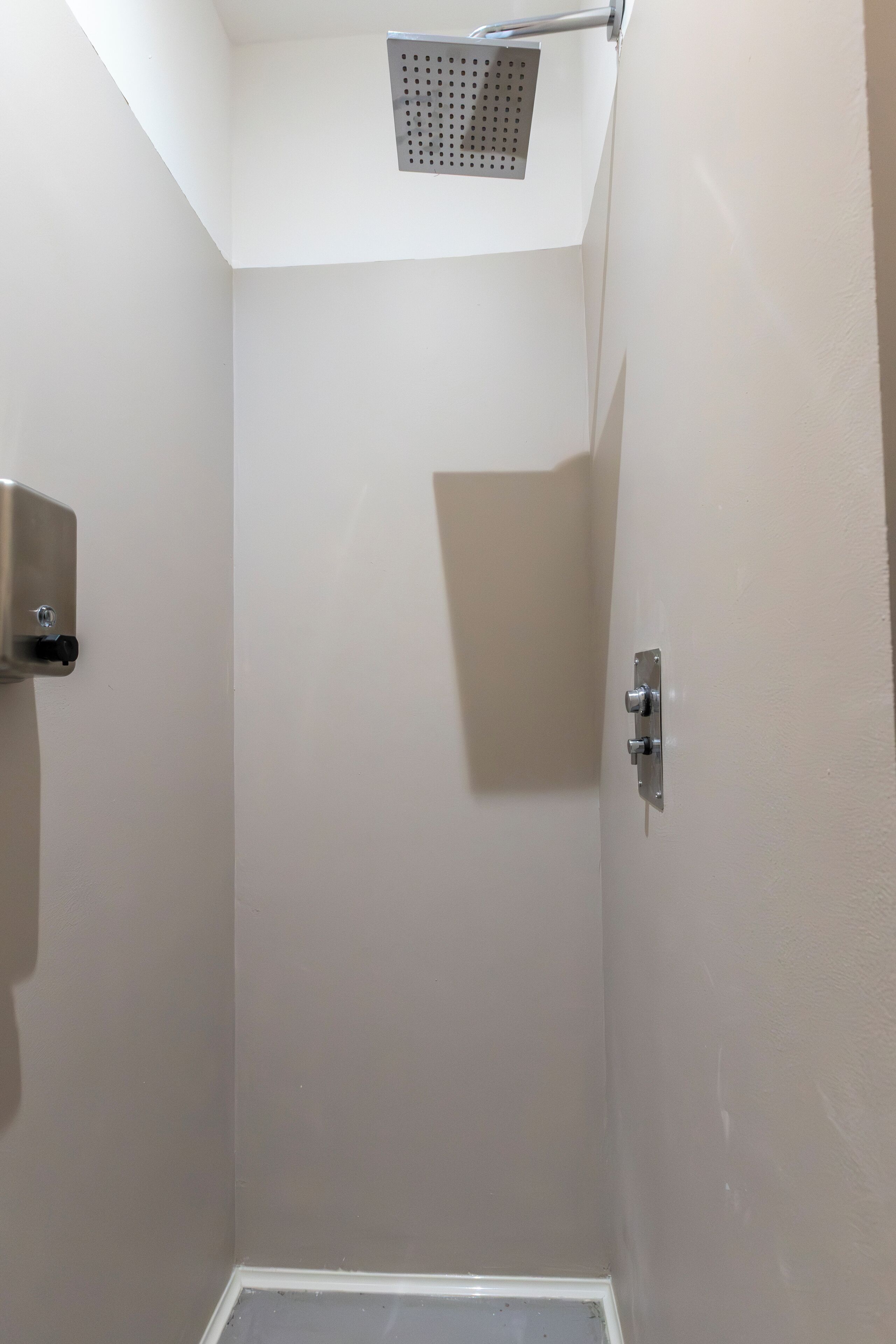 Un petit espace de douche fermé, équipé d’un pommeau de douche et d’un panneau de commande fixé au mur.
