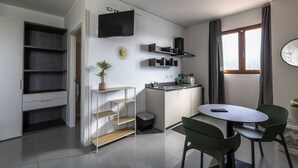 Cozinha moderna com eletrodomésticos embutidos, área de jantar com mesa e cadeiras e uma TV fixada na parede.