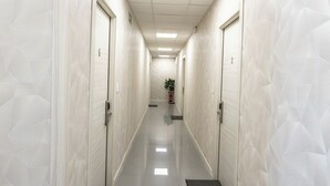 Corredor com paredes e portas brancas, um extintor e uma luminária no teto.
