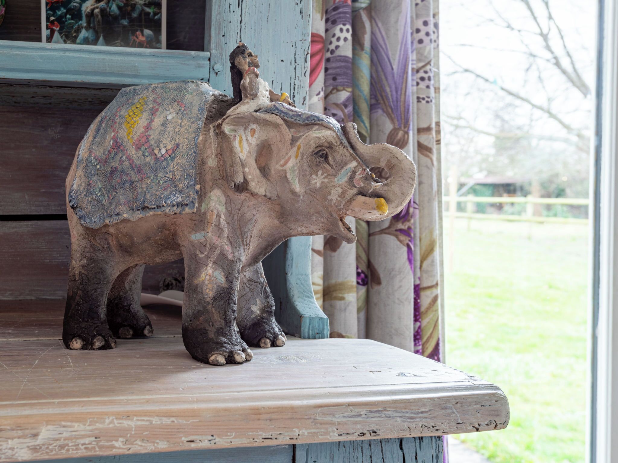 A rustic elephant sculpture with a human figure on its back, placed on a wooden platform.