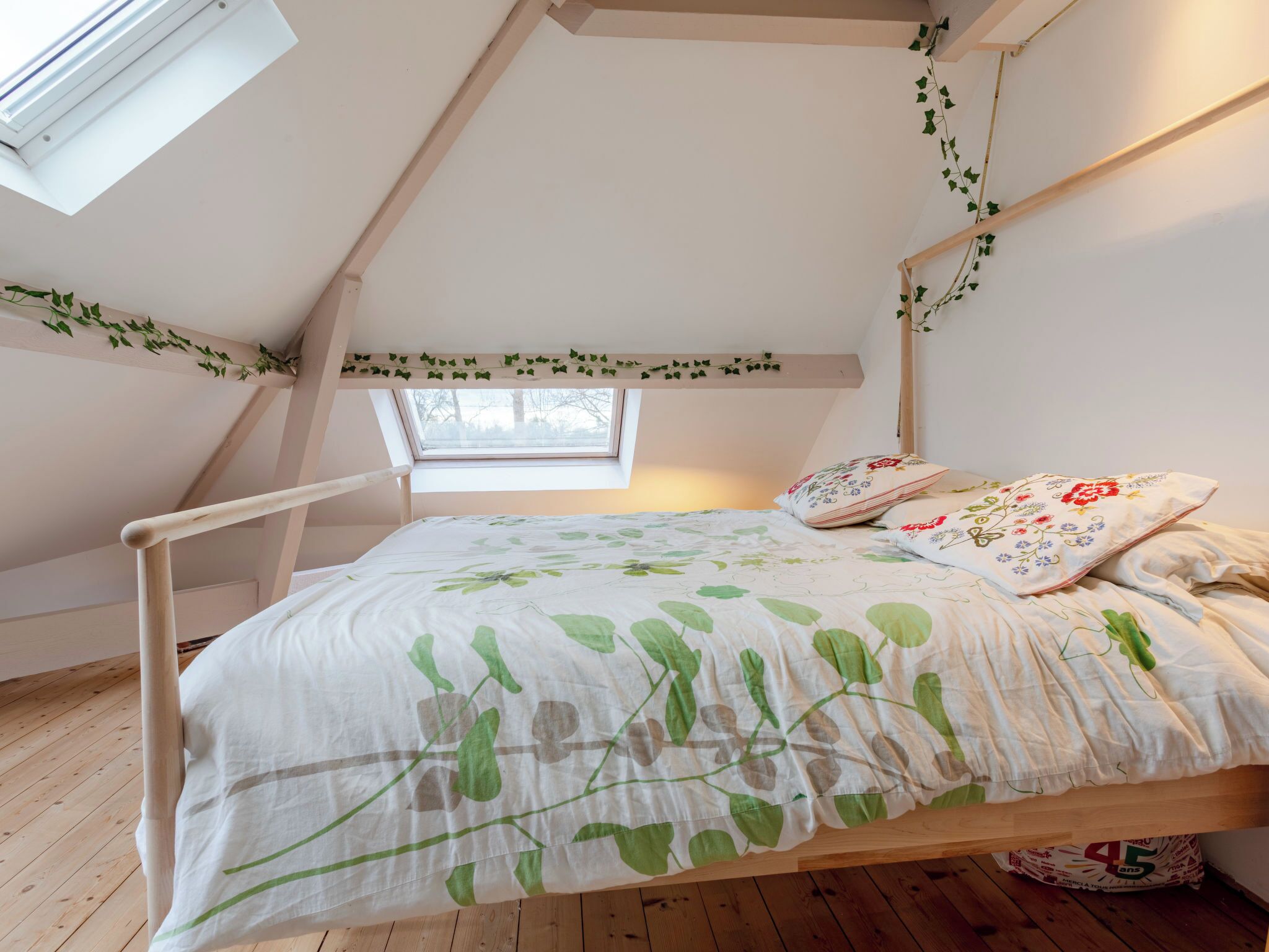 A bedroom with a sloped ceiling, a skylight, a bed with a floral bedspread, and a wooden headboard.