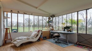 A sunroom with a large window, a cushioned bench, a desk with a chair, and a wooden floor. - La maison du cavalier bleu by Interhome (Deauville-Trouville)