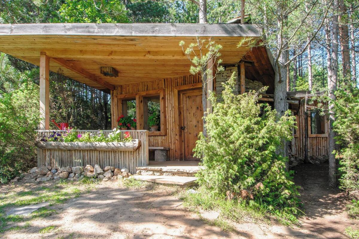 Un chalet rustique doté d’un porche en bois, d’un escalier en pierre et d’un petit jardin agrémenté de fleurs.
