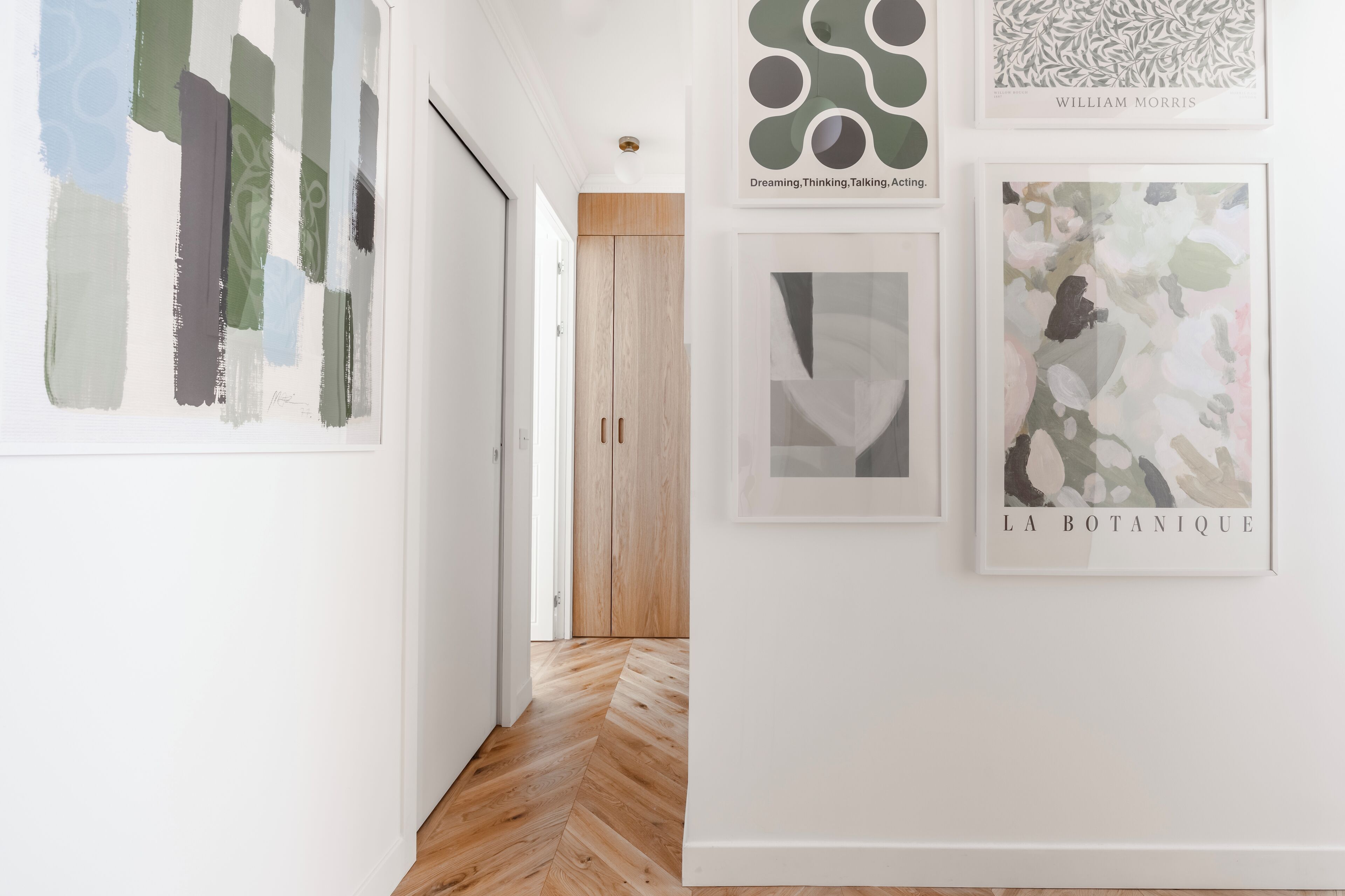 A hallway with a wooden floor, white walls, and framed artwork.