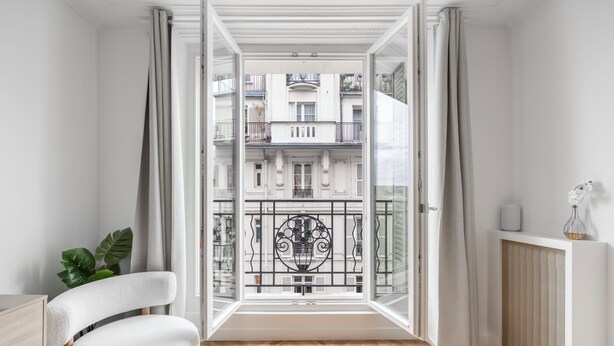 A modern apartment with a large window, a white chair, a radiator, and a potted plant. - We Parisian * Invalides* Cozy Home (Paris)