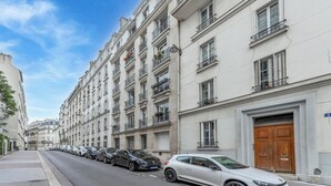A row of parked cars along a street lined with multi-story buildings with balconies and a large wooden door. - We Parisian * Invalides* Cozy Home (Paris)