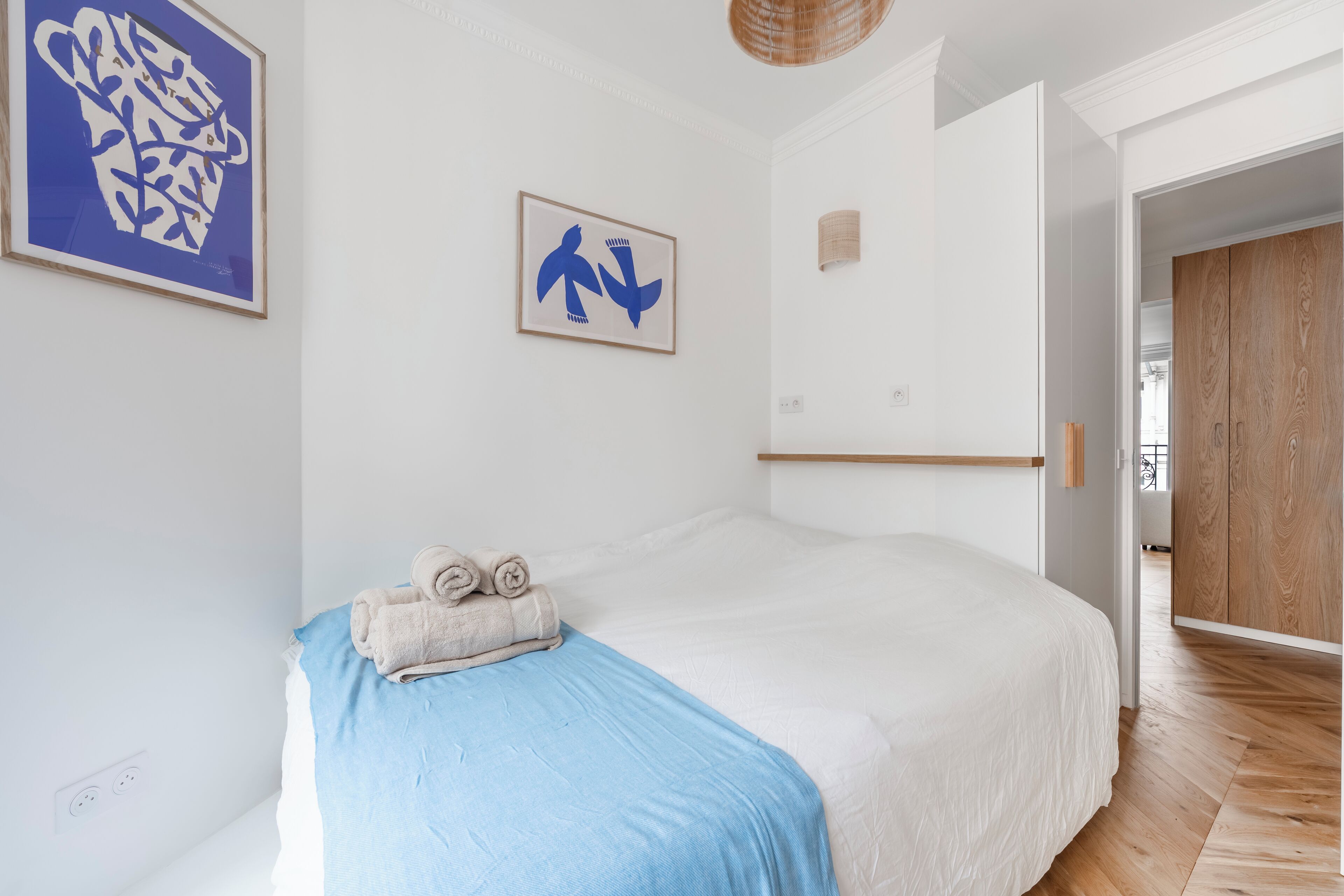 Ein Schlafzimmer mit einem großen Bett, einer blauen Decke und zwei Handtüchern auf dem Bett. An der Wand hängen zwei gerahmte Kunstwerke.