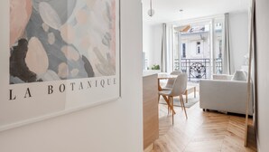 A modern living room with a herringbone wooden floor, a white sofa, a dining table with chairs, and a large abstract painting on the wall. - We Parisian * Invalides* Cozy Home (Paris)