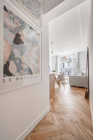 A modern living room with a herringbone wooden floor, a white sofa, a dining table with chairs, and a large abstract painting on the wall. - We Parisian * Invalides* Cozy Home (Paris)