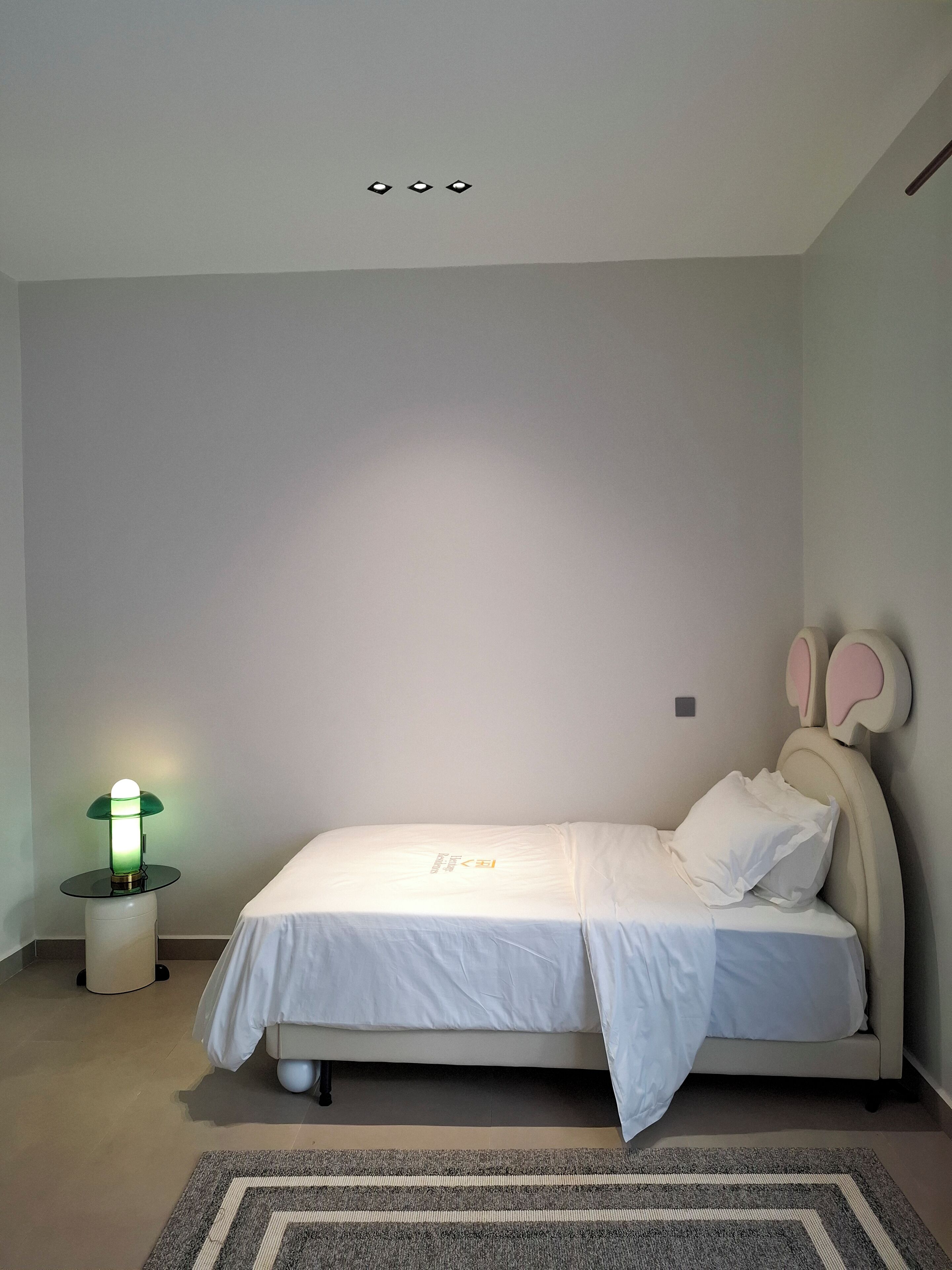A bedroom with a bed, a bedside lamp, and a headboard with a bunny design.