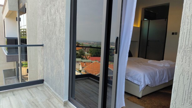 Un balcon doté d’une porte-fenêtre coulissante donnant sur une chambre à coucher avec un lit et une vue sur le paysage urbain.