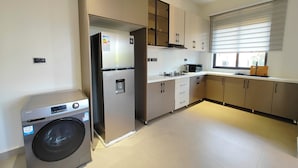 Une cuisine moderne équipée d’appareils électroménagers en acier inoxydable, d’un lave-linge intégré et d’une fenêtre avec des stores.