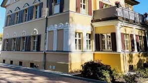 A two-story building with a symmetrical facade, multiple windows with shutters, and a balcony on the upper floor.