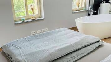 Ein modernes Badezimmer mit freistehender Badewanne, einem großen Fenster mit Jalousien und einem wandmontierten Spiegel.