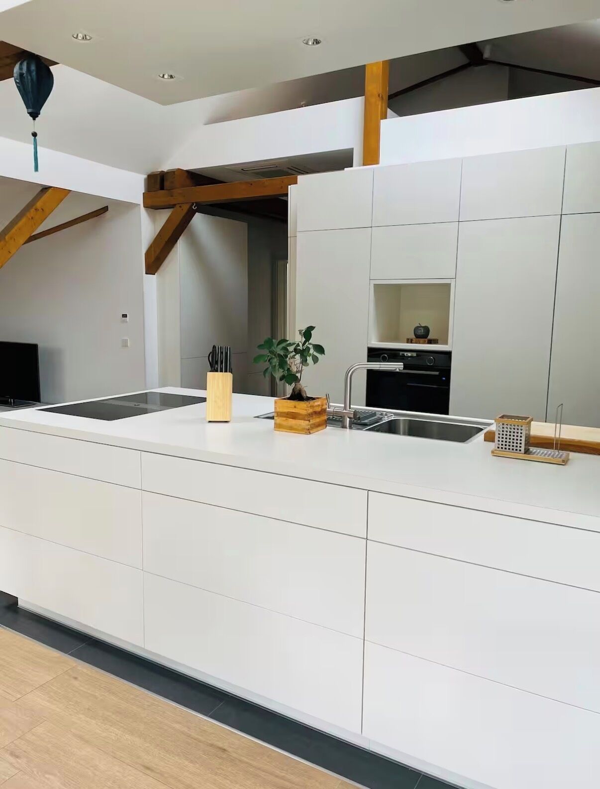 A modern kitchen with white cabinetry, a wooden ceiling beam, a built-in sink, and a small plant on the counter.