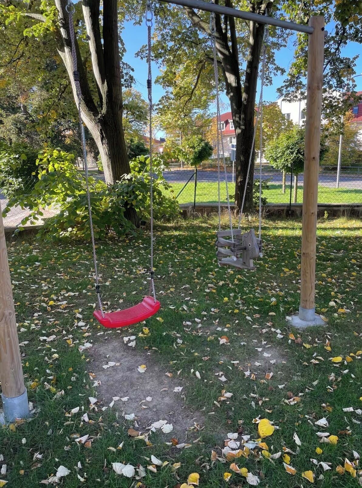 Ein Park mit Schaukeln, Bäumen und einer Rasenfläche mit herabgefallenen Blättern.