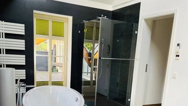 A modern bathroom with a freestanding bathtub, a glass shower enclosure, and a large window.