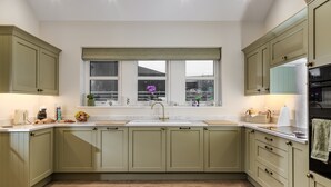 Een keuken met groene kastjes, een wit aanrecht, een raam met jaloezieën en een spoelbak.