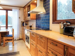 A kitchen with wooden cabinets, a stove, a toaster, and a window with a view of trees. - 6 Person Holiday Home in Hunnebostrand (Kungshamn)