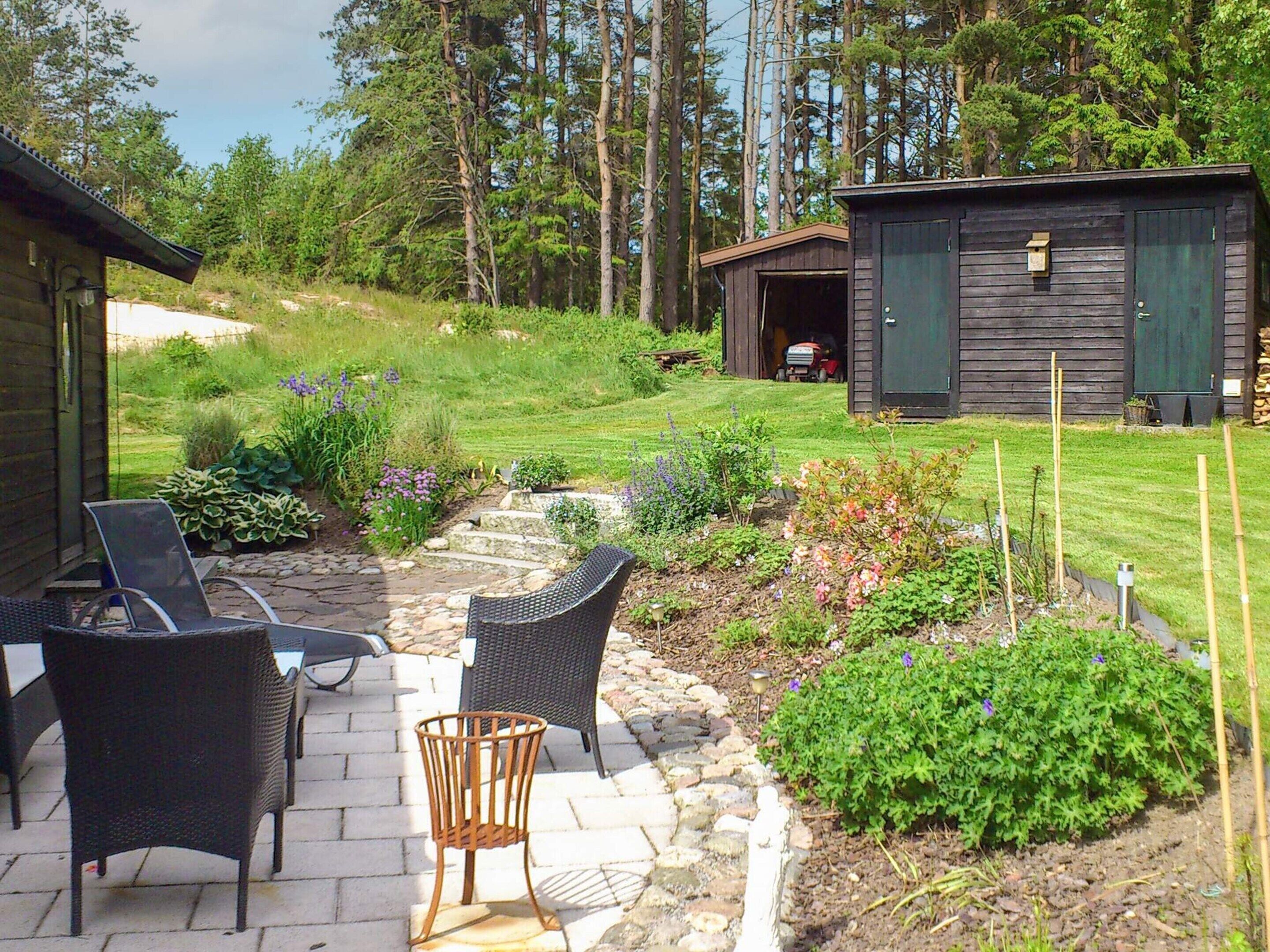 Eine Terrasse mit Korbmöbeln, einem Steinweg und einem kleinen Garten mit verschiedenen Pflanzen.