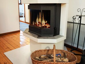 A fireplace with visible flames, a basket of firewood, and a metal stand with a hook. - 6 Person Holiday Home in Hunnebostrand (Kungshamn)
