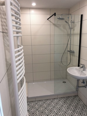 A modern bathroom with a glass-enclosed shower, a white sink, and patterned floor tiles. - Vacation apartment in the countryside (Herleshausen)