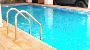 An indoor swimming pool with a metal ladder and wooden deck. - Sterling Suites (Accra)