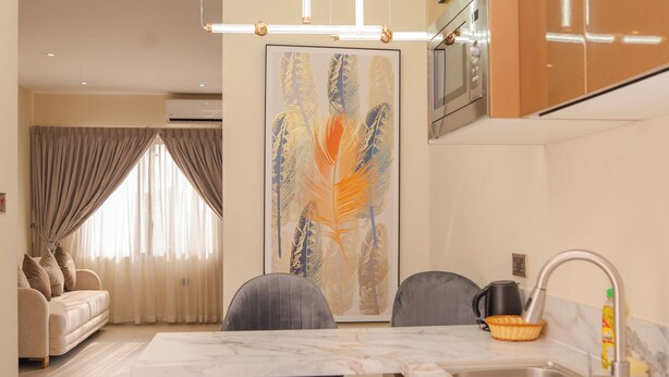 A modern kitchen with a built-in washing machine, a dining area with a table and chairs, and a living room with a sofa and curtains. - Sterling Suites (Accra)