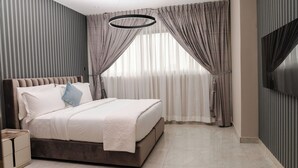 A modern bedroom with a large bed, a TV mounted on the wall, and a large window with curtains. - Sterling Suites (Accra)