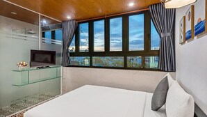 A bedroom with a bed, a TV on a glass shelf, a shower, and large windows with curtains. - Dory Hotel (Hoi An)