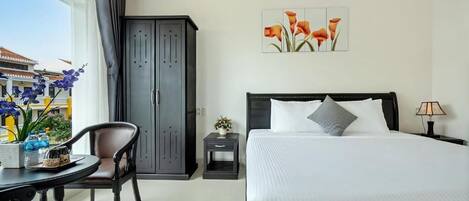 A hotel room with a bed, a desk, a chair, a wardrobe, and a window with a view of buildings.