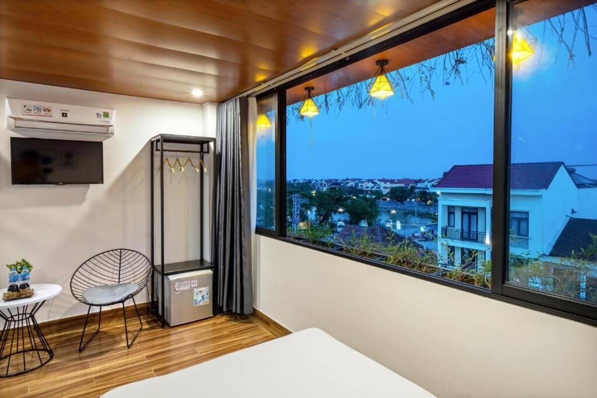 Une chambre moderne dotée d’une grande fenêtre, d’un climatiseur intégré, d’une petite table avec une chaise et d’un meuble de rangement compact.