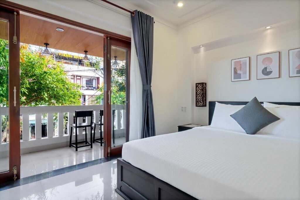 A hotel room with a large bed, a balcony with a view of the city, and a small table with chairs.