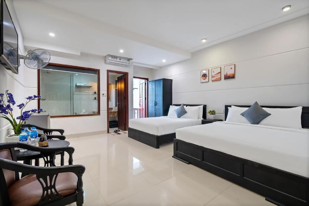 A hotel room with two beds, a desk with chairs, a TV, and a large window.