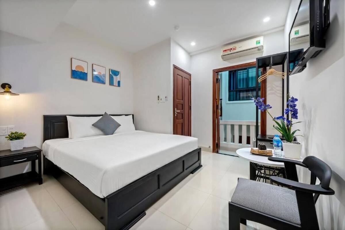 Une chambre moderne avec un grand lit, une table de chevet et un petit bureau avec une chaise. Elle dispose d’un balcon avec vue sur l’extérieur.