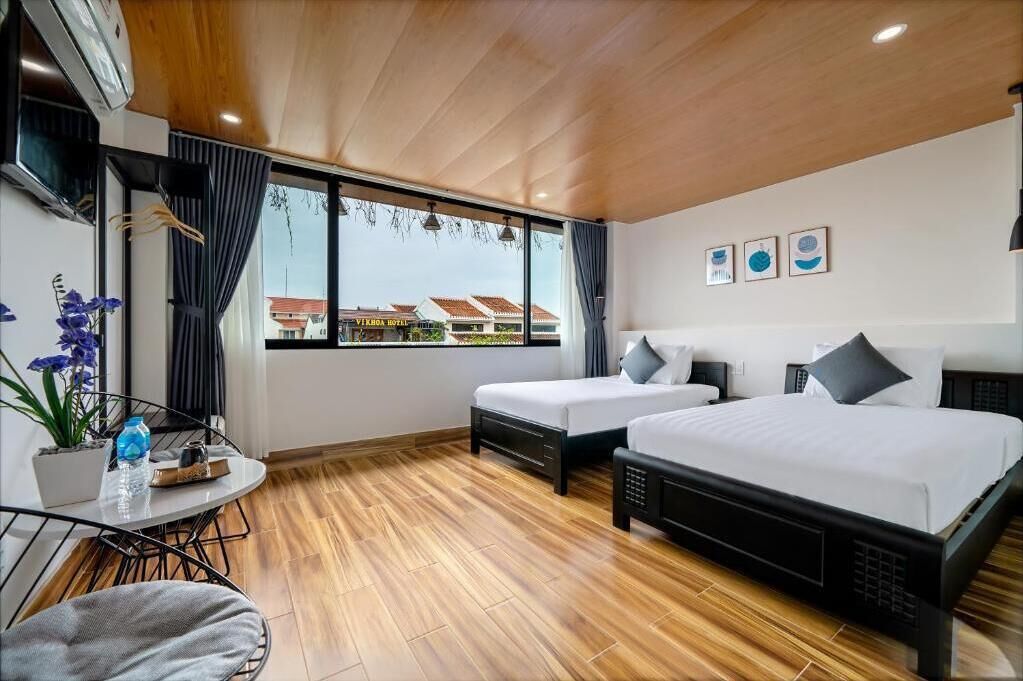 Une chambre d’hôtel avec deux lits, une petite table et une fenêtre donnant sur des immeubles.