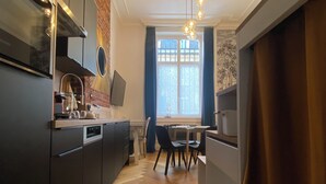 A modern kitchen with dark cabinetry, a dining area with a table and chairs, and a large window with curtains.