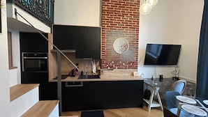 A modern kitchen with a brick accent wall, a dining area with a glass table, and a TV mounted on the wall.