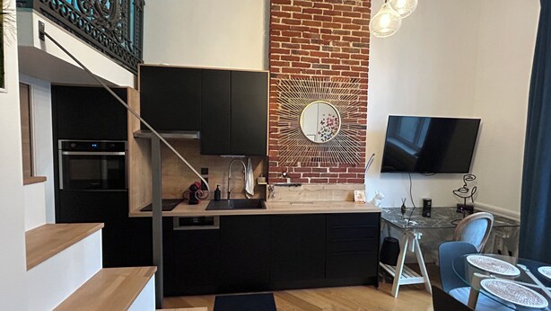 Une cuisine moderne avec un mur d’accent en briques, un coin repas doté d’une table en verre et un téléviseur fixé au mur.