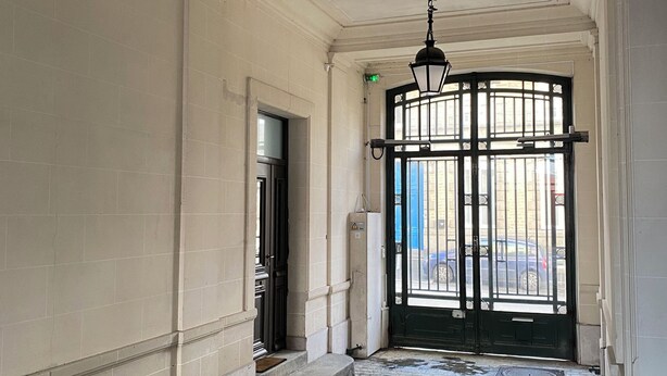 A corridor with a cobblestone floor, white walls, and a black gate with decorative glass panels.
