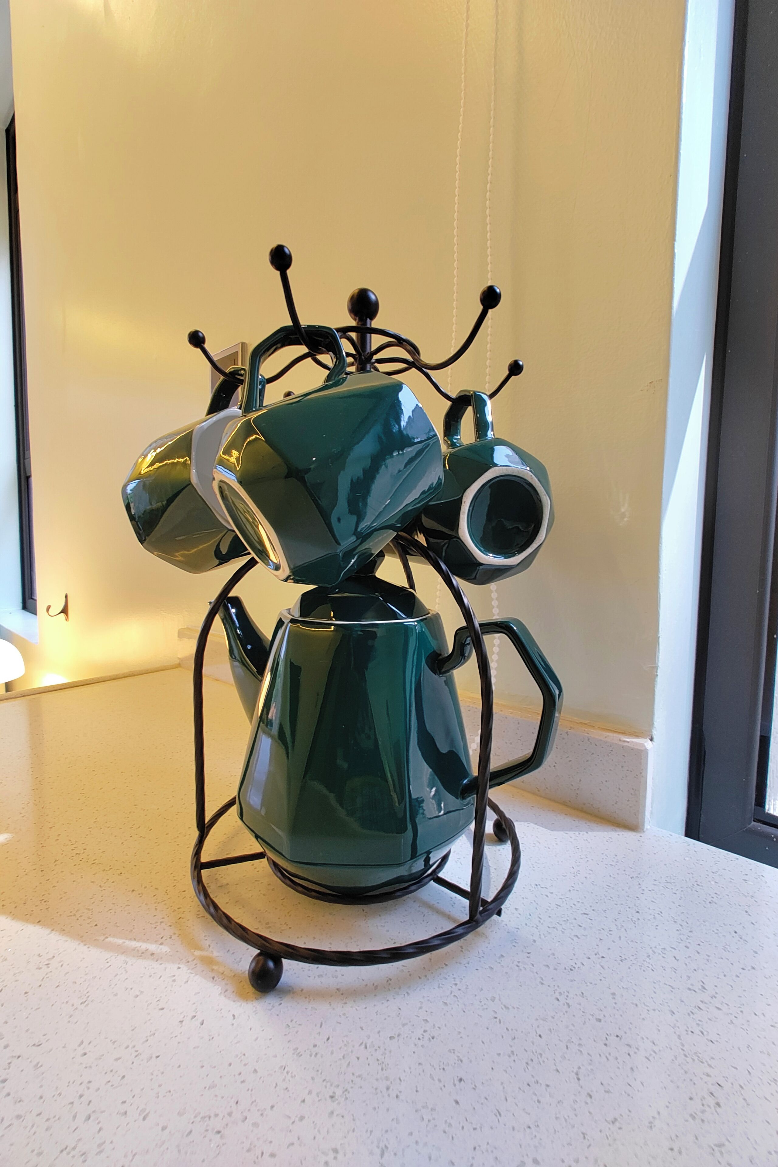 A green, metallic, futuristic-looking object with multiple protruding elements, possibly a decorative piece or a piece of modern art, placed on a white countertop.