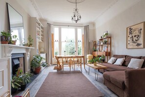 A living room with a fireplace, a dining table, a sofa, and a chandelier. - Refined 2BDR Family Retreat with Garden in Clapham (Greater London)
