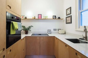 A kitchen with wooden cabinets, a built-in oven, a sink, and a countertop. - Refined 2BDR Family Retreat with Garden in Clapham (Greater London)