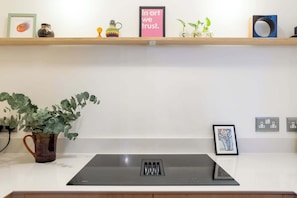 A kitchen with a black induction cooktop, a potted plant, and a shelf with various decorative items. - Refined 2BDR Family Retreat with Garden in Clapham (Greater London)