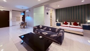 Una habitación de hotel moderna con sofá, cama con almohadas rojas, mesita de noche y escritorio con silla.