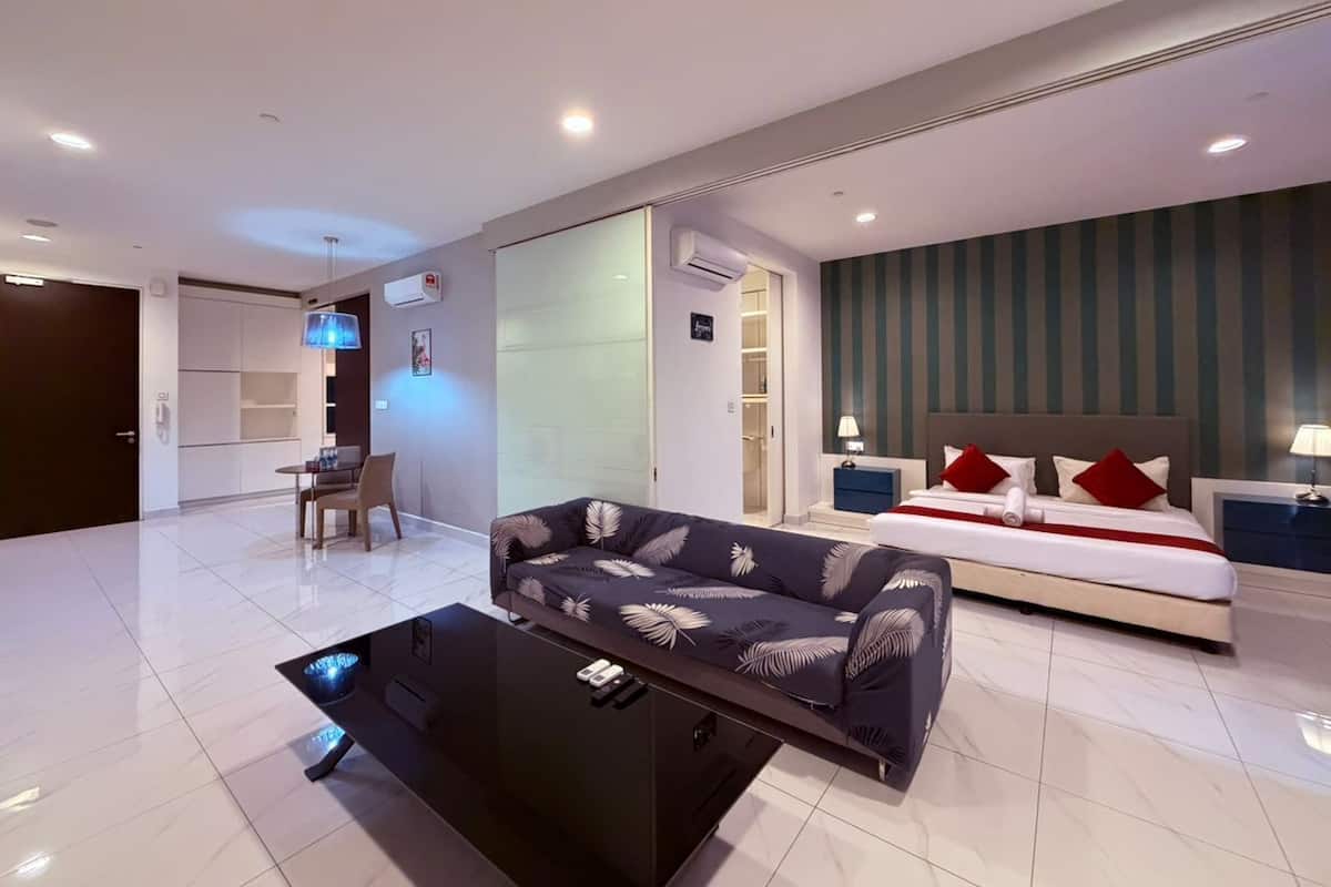 A modern hotel room with a sofa, a bed with red pillows, a bedside table, and a desk with a chair.