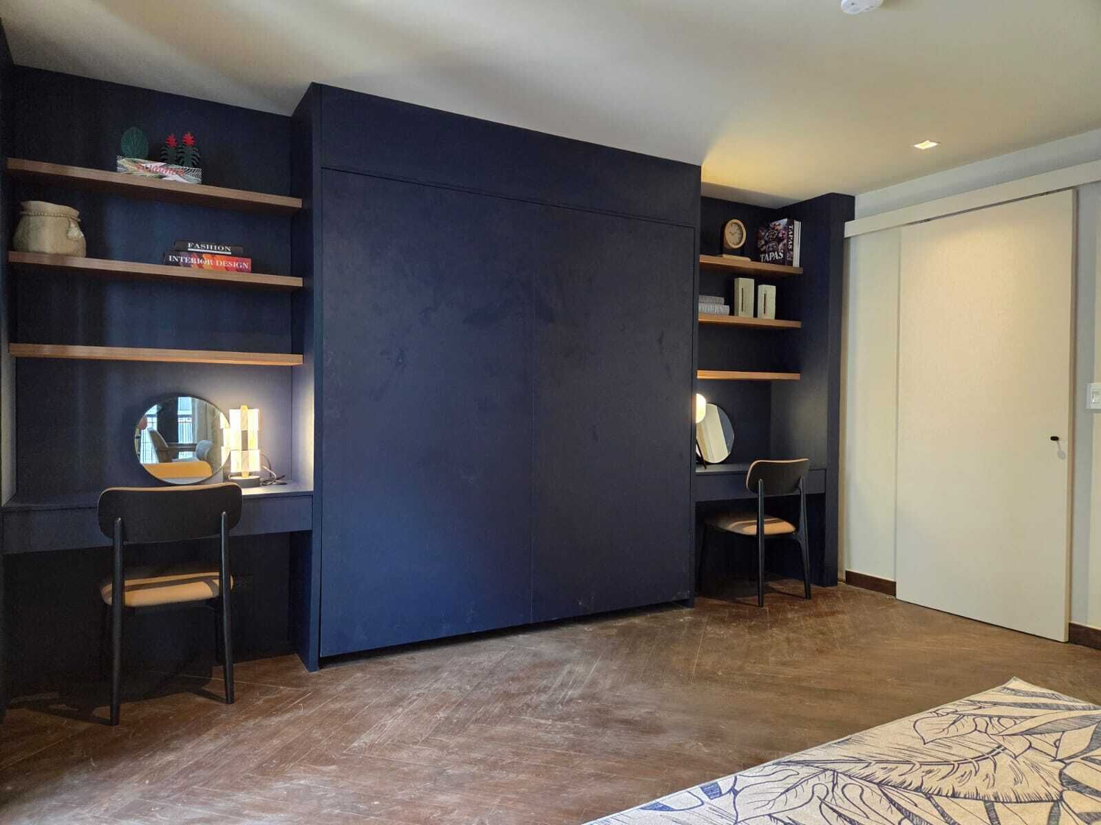 Een moderne kamer met een donkerblauwe schuifdeur, houten planken met boeken en decoratieve objecten, twee stoelen en een kamerbreed tapijt met een patroon.