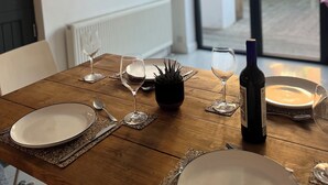 A dining table set with plates, glasses, and a bottle, with a view of a garden outside.