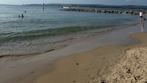 A beach with clear water, a rocky breakwater, and footprints in the sand.