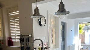 A kitchen with a double sink, hanging utensils, and a clock on the wall.